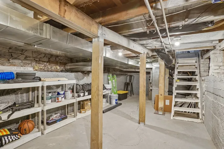 Unfinished basement with concrete flooring, exposed wood beams, and a concrete block foundation