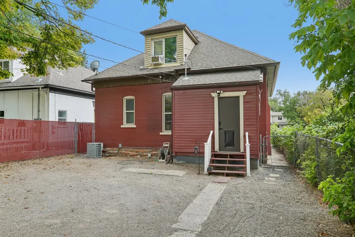 Red brick and siding exterior with a dormer window, gravel ground cover, and a chain link fence