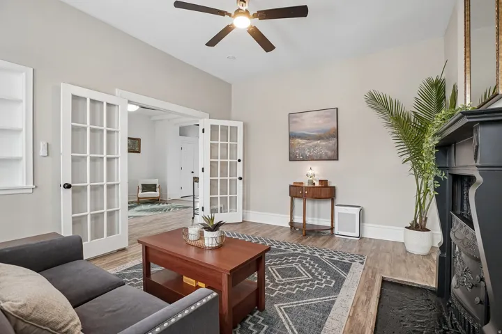 Light gray wall paint, wood-finish flooring, built-in shelving, glass-paned French doors, and a black ceiling fan