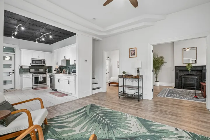 Open-concept living space featuring wood-finish flooring, a contemporary kitchen with white cabinetry and stainless steel appliances, and a decorative fireplace