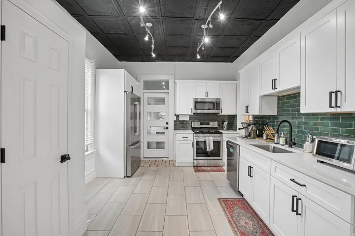 Modern kitchen featuring white cabinetry with hardware accents, stainless steel appliances including a gas range and microwave, tile countertops, subway tile backsplash in soft green, and tile flooring throughout