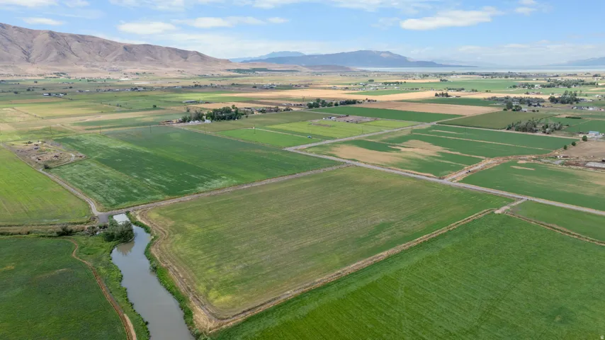 Expansive agricultural fields with varied crops, a winding river, and distant mountains