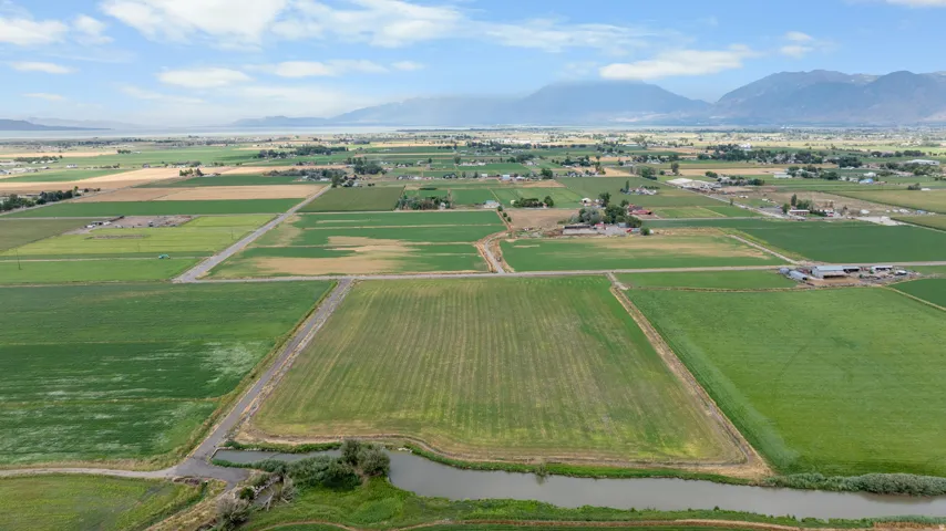 Expansive agricultural land featuring cultivated fields, a meandering waterway, distant mountains, and a clear sky