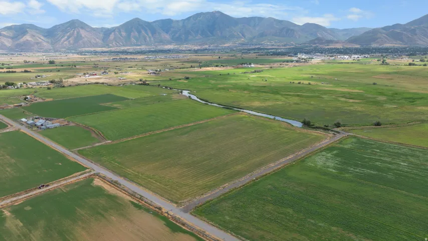 Expansive agricultural land featuring a winding river, mature green fields, and distant mountains