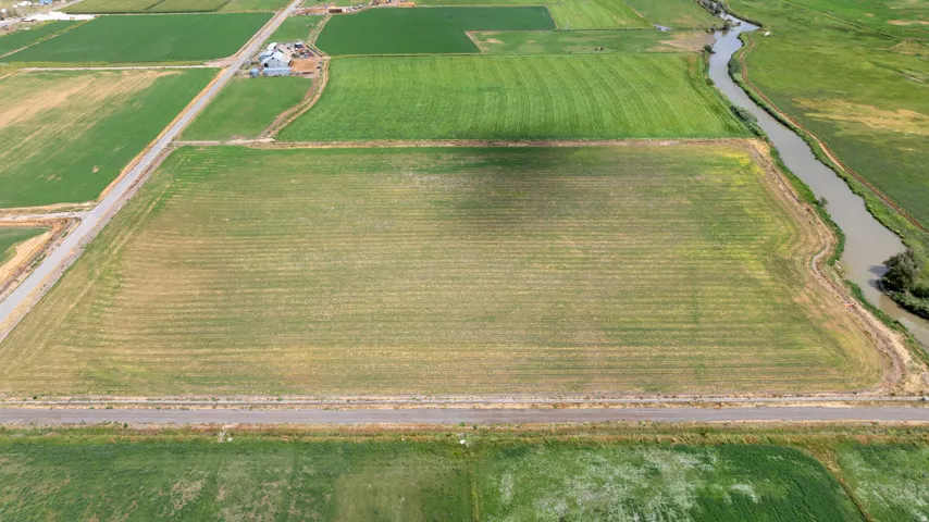 Expansive agricultural land featuring cultivated fields, a meandering waterway, and adjacent paved roadways