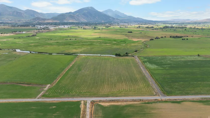 Expansive agricultural land featuring a waterway, green fields, and distant mountains