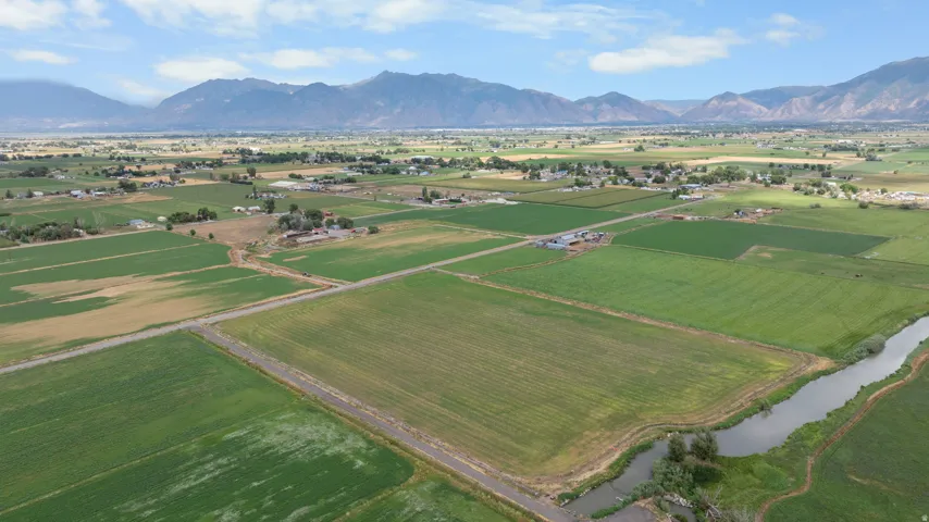 Expansive agricultural land featuring cultivated fields, a natural waterway, and distant mountainous terrain
