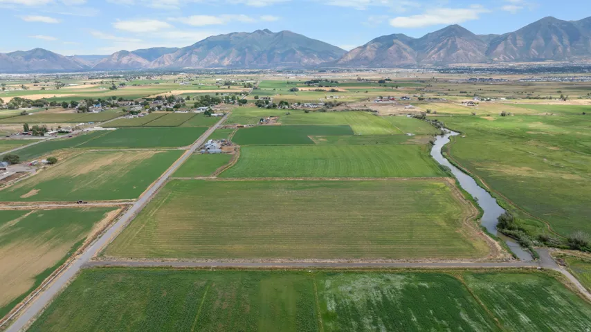 Expansive agricultural land featuring a meandering river, mountain backdrop, and clear skies