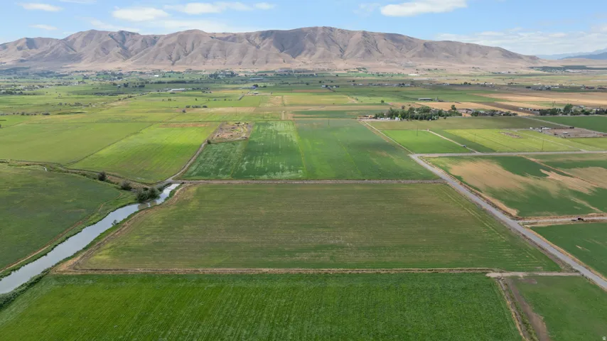 Expansive agricultural landscape featuring diverse cultivated fields, a winding waterway, and a prominent mountain range in the background
