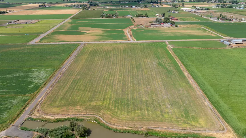 Expansive agricultural land featuring cultivated fields, a defined access road, and an adjacent water feature
