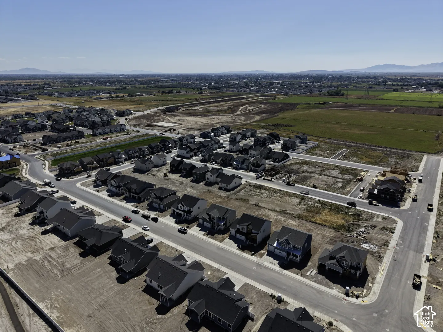 Newly developed residential community with paved streets and established homes, set against a backdrop of distant mountains and agricultural land