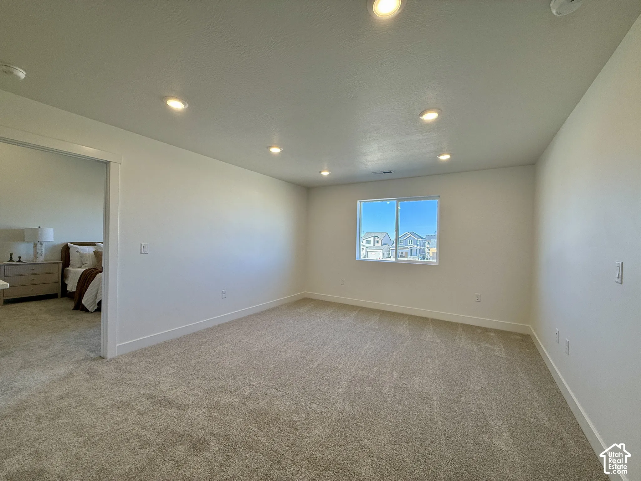 Spacious room featuring neutral carpeting, recessed ceiling lighting, and a single-pane sliding window