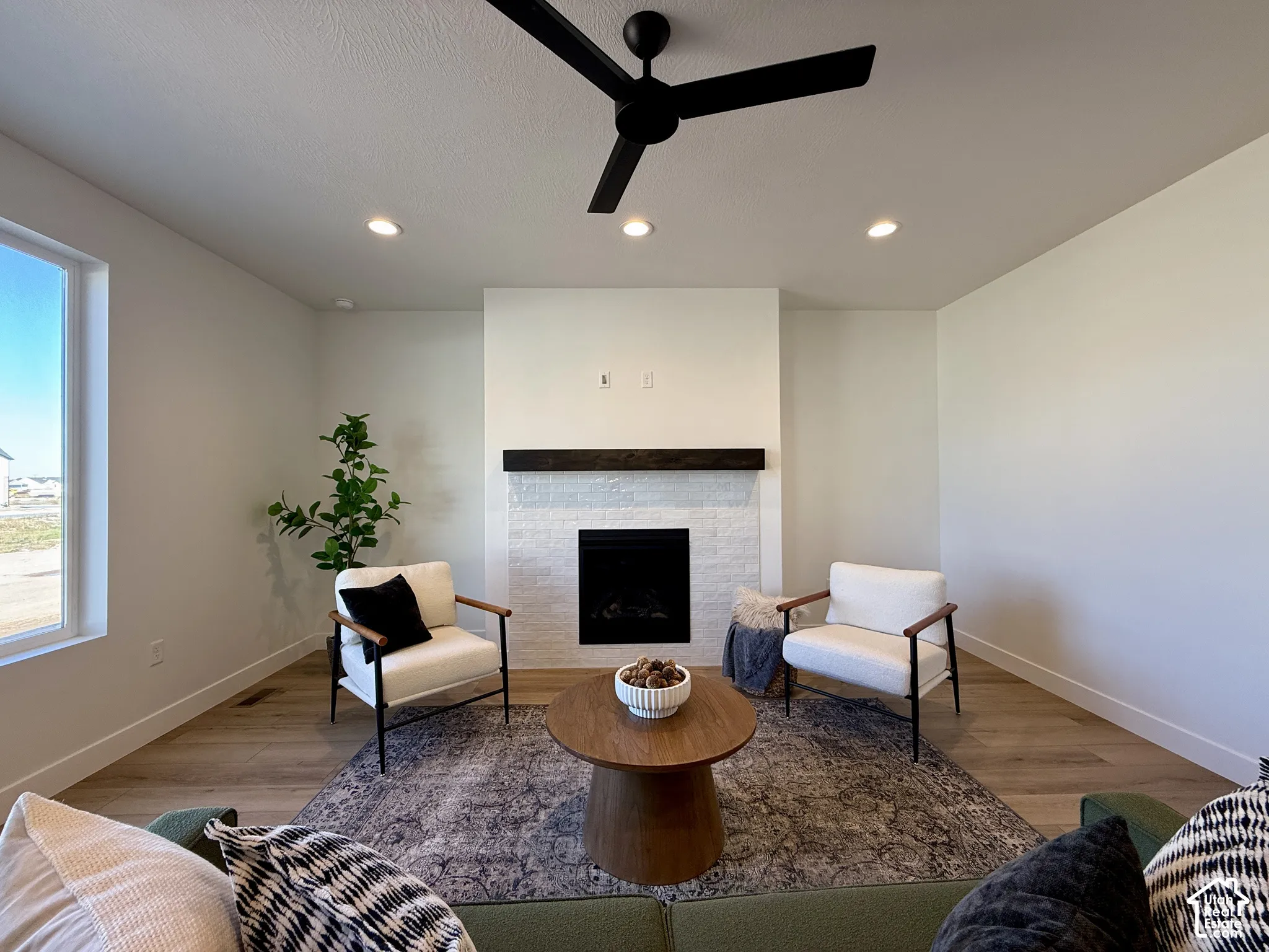 Fireplace featuring a white-painted brick surround and a dark wood mantel, recessed lighting, matte black ceiling fan, and wood-finish flooring