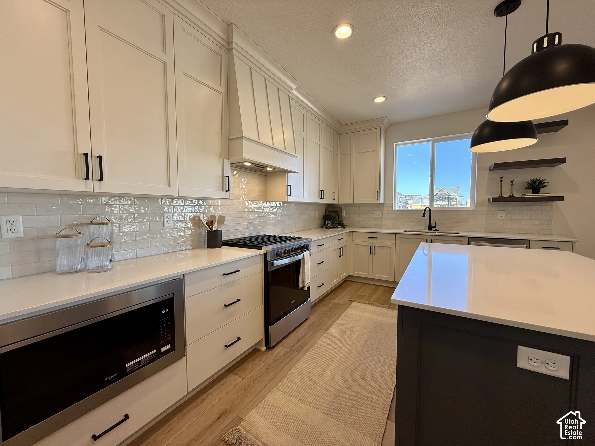Kitchen featuring white cabinetry, quartz countertops, subway tile backsplash, stainless steel appliances, and a dark-toned center island with pendant lighting