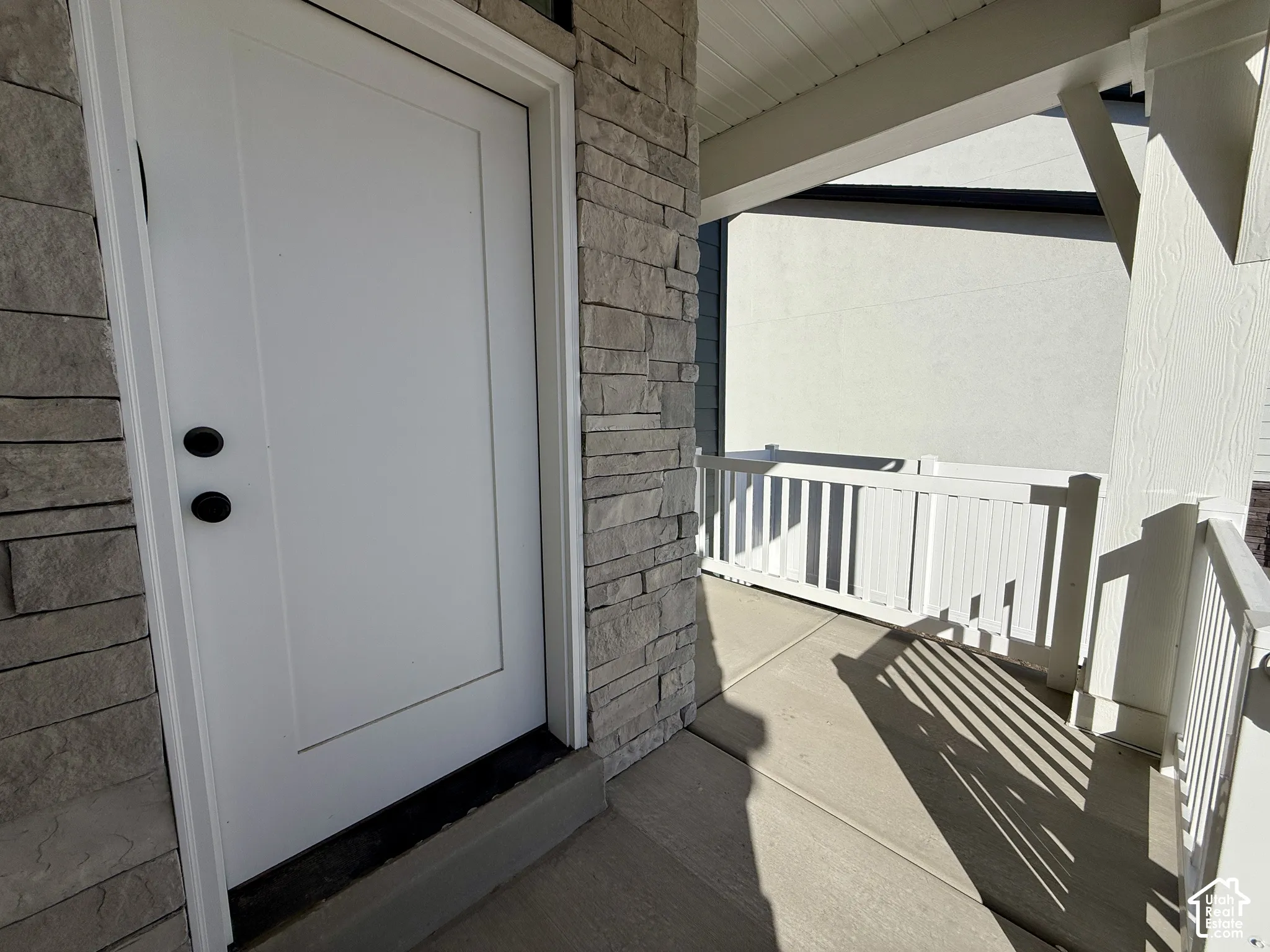 Covered entryway featuring a white panel door with matte black hardware, stone veneer siding, and a white picket-style railing