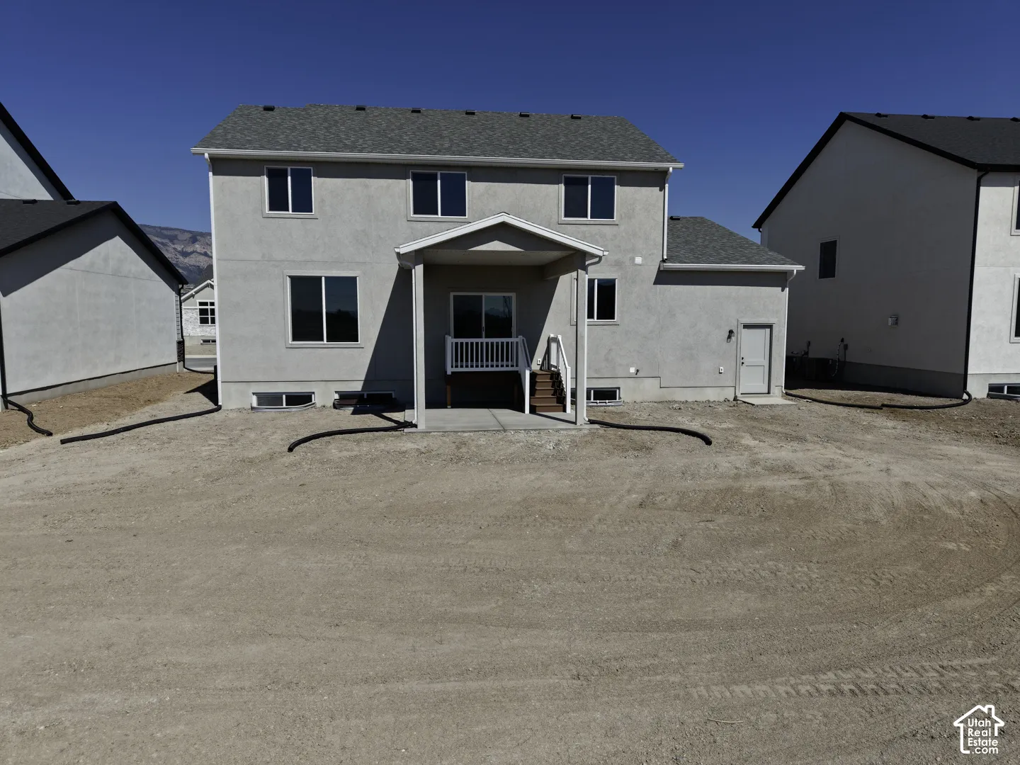 Two-story property featuring a covered patio with railing, a walk-out basement, and a light-colored stucco exterior