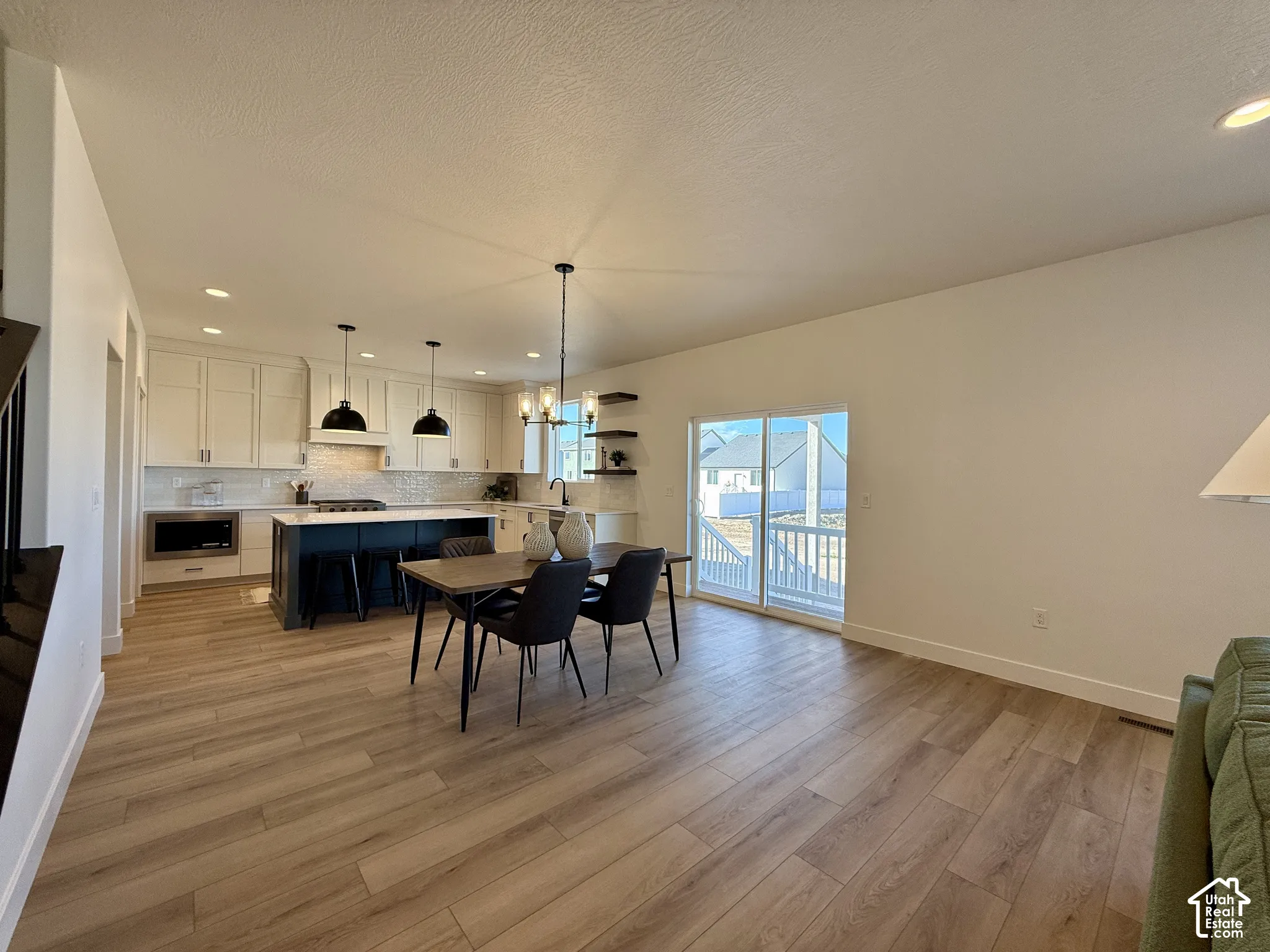 Open-concept interior featuring wood-finish flooring, a kitchen island with built-in cabinetry, dual pendant lighting, and a sliding glass door