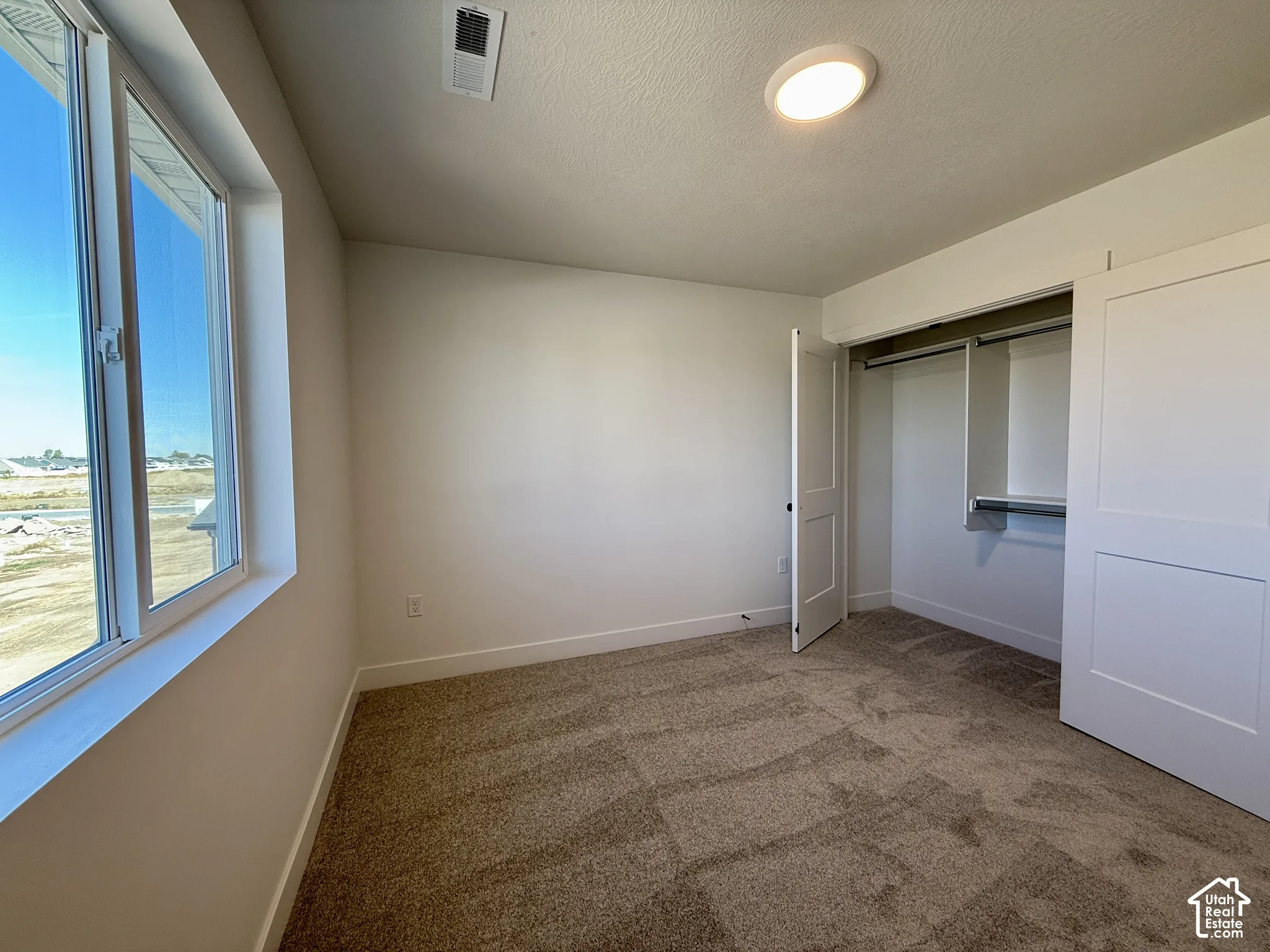 Neutral-toned carpeting, large window, and closet with built-in shelving