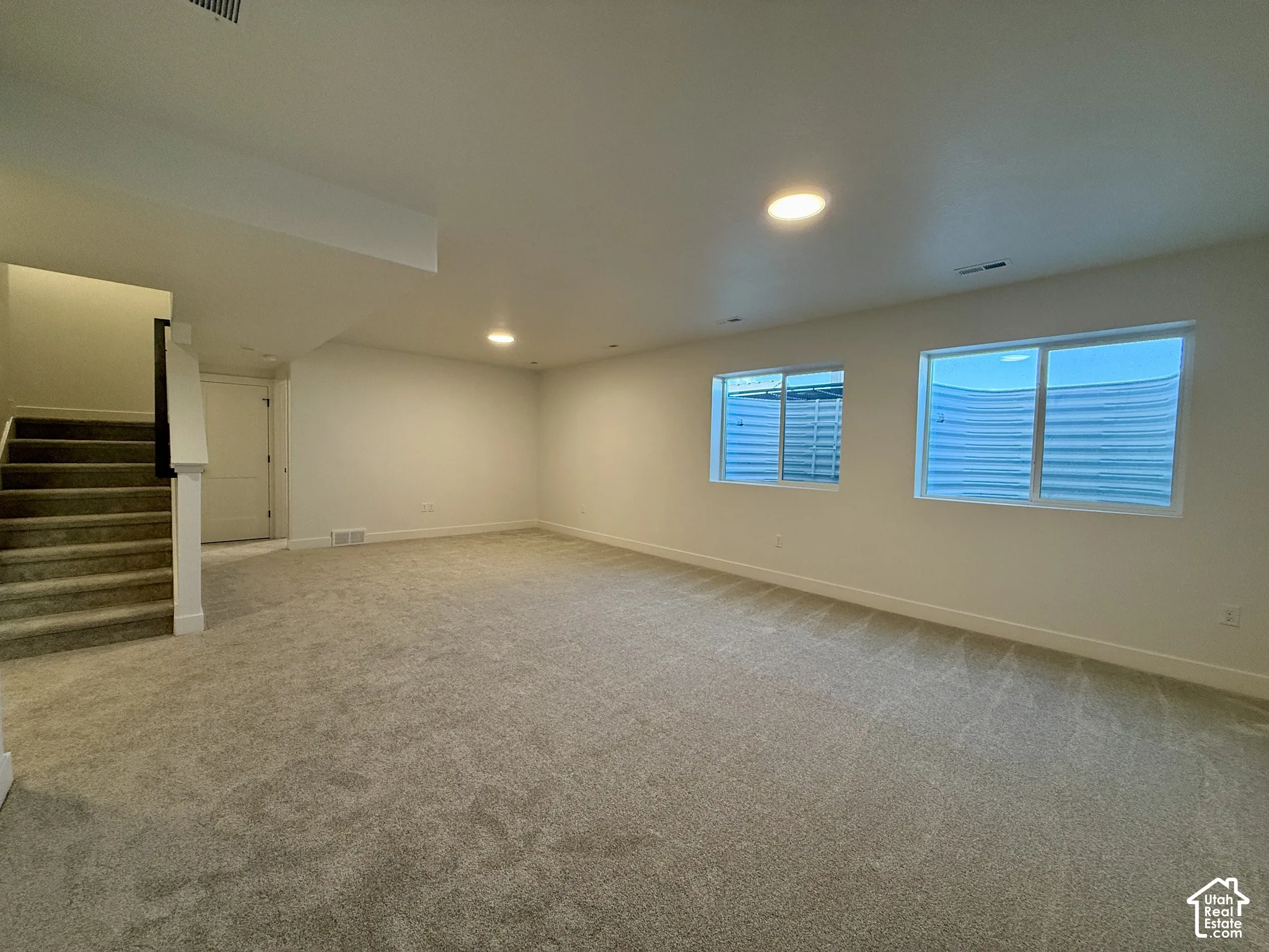 Open floor plan interior featuring wall-to-wall carpeting, recessed ceiling lighting, and multiple sliding windows with exterior window wells