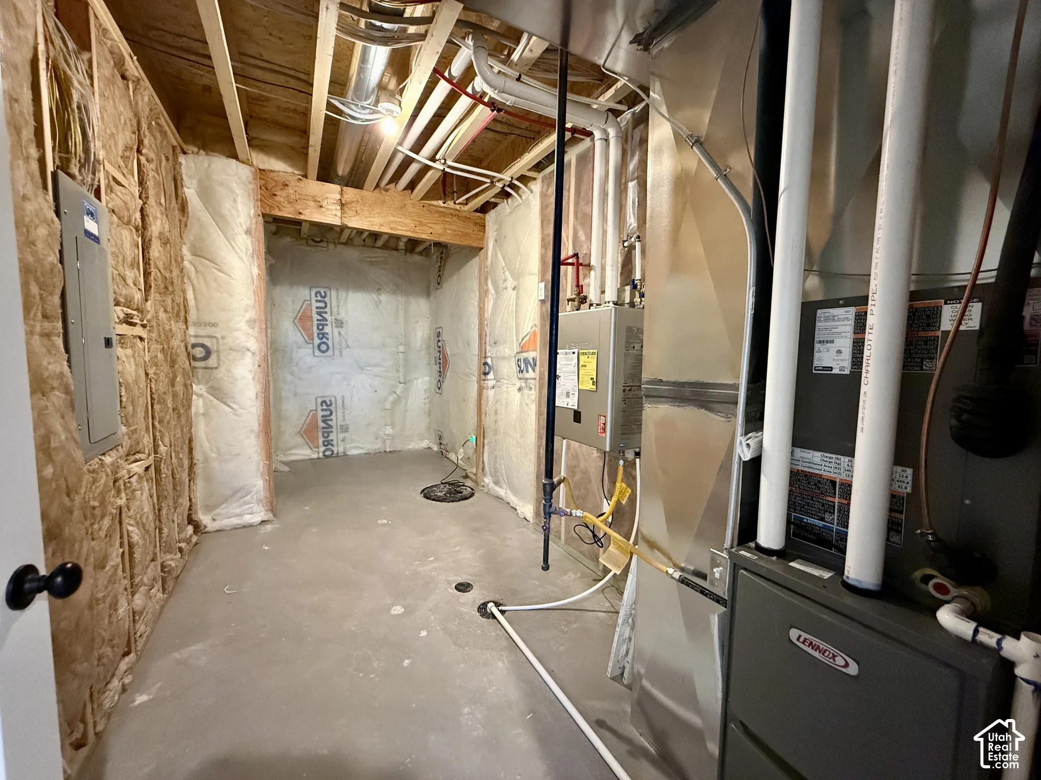 Mechanical area featuring a concrete floor, fiberglass-insulated wall studs, a wall-mounted tankless water heater, and a high-efficiency furnace
