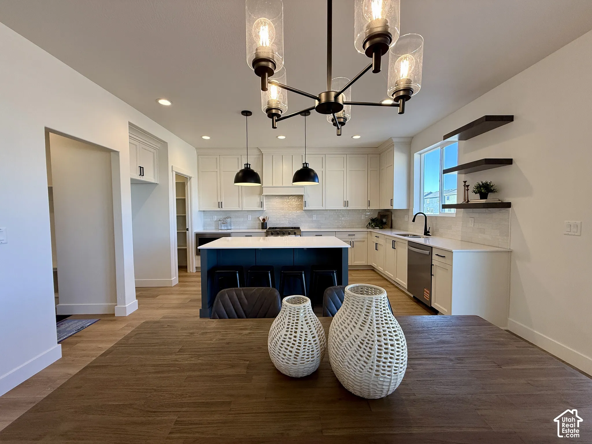 Kitchen featuring white cabinetry, center island with stone-finish countertop, wood-finish flooring, matte black pendant lighting, and floating wood shelving
