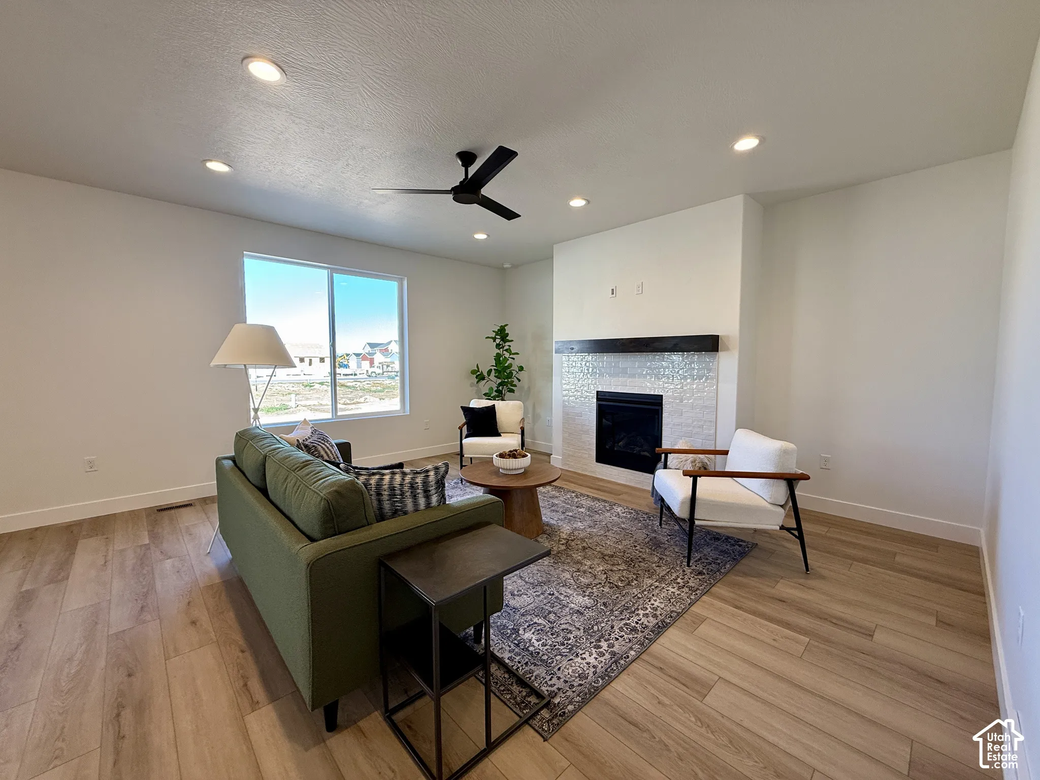Living area featuring wood-finish flooring, recessed lighting, ceiling fan, and a fireplace with a textured tile surround and a dark wood mantel