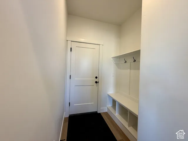 Built-in mudroom bench with open cubbies, white wall paneling, overhead shelf, and matte black hardware hooks