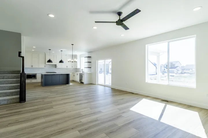 Open-concept main level featuring wood-finish flooring, a kitchen with a dark-toned island and white cabinetry, recessed lighting, and a black ceiling fan