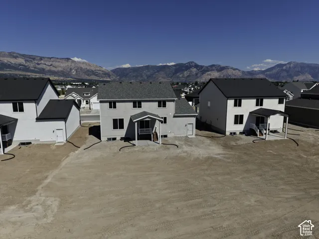 Expansive lot with a mountain backdrop, featuring a stucco-finish exterior and a covered patio