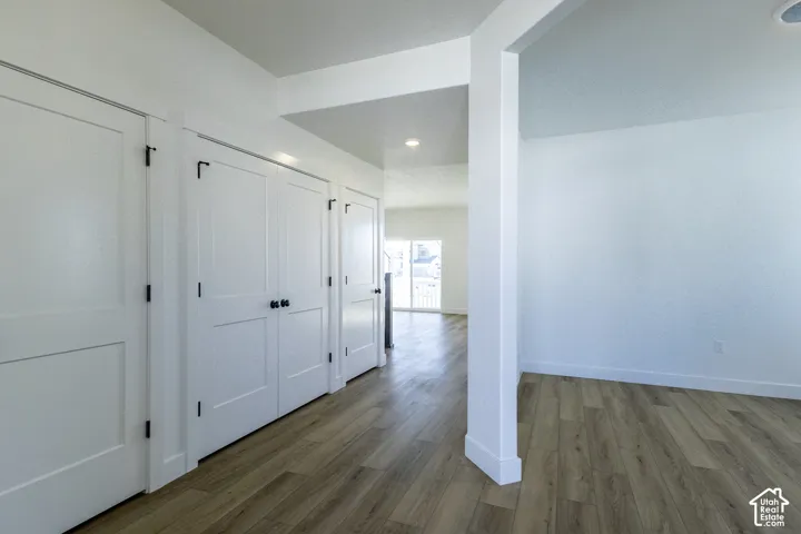 Bright, open hallway featuring white panel doors with black hardware, polished wood-finish flooring, and clean architectural lines accented by white trim and support columns