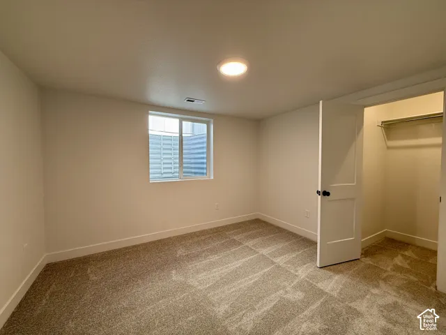 Neutral-toned carpeting, flush-mount ceiling lighting, sliding egress window with metal window well, and interior closet featuring a built-in shelving rod