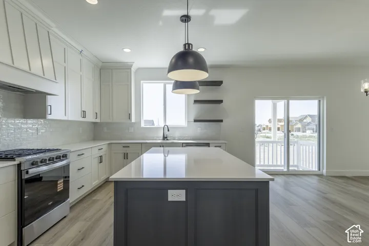 Spacious kitchen featuring an expansive island, white shaker cabinetry, stainless steel range, and light wood-finish flooring