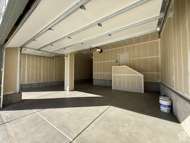 Spacious multi-car garage featuring a concrete floor, overhead door mechanism, and drywall-finished walls with a built-in partition structure