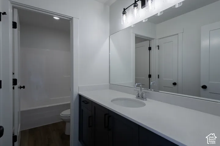 Modern primary bathroom featuring a dark cabinetry vanity with an expansive white quartz countertop, single-basin sink with chrome faucet, and frameless mirror with integrated lighting
