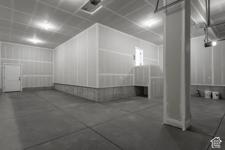 Concrete flooring, interior access door, recessed lighting, exposed garage door mechanism, and a built-in workbench area