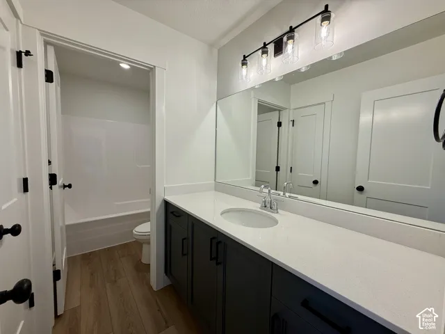 Bathroom featuring dark charcoal cabinetry, white quartz countertop with an integrated basin, large wall-mounted mirror, three-light fixture with cylindrical glass shades, and wood-finish flooring