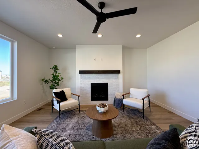 Fireplace featuring a white-painted brick surround and a dark wood mantel, recessed lighting, matte black ceiling fan, and wood-finish flooring