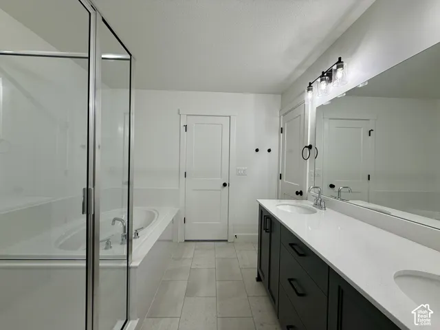 Double-sink vanity with dark cabinetry, quartz countertops, soaking tub, glass-enclosed shower, and large-format tile flooring