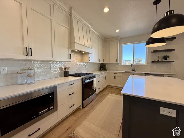 Kitchen featuring white cabinetry, quartz countertops, subway tile backsplash, stainless steel appliances, and a dark-toned center island with pendant lighting