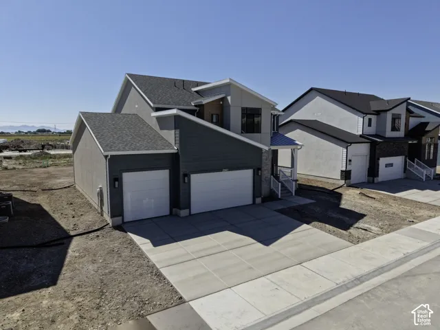 Modern two-story residence featuring a spacious three-car garage with white panel doors, concrete driveway, and clean architectural lines with mixed exterior finishes in gray and white tones