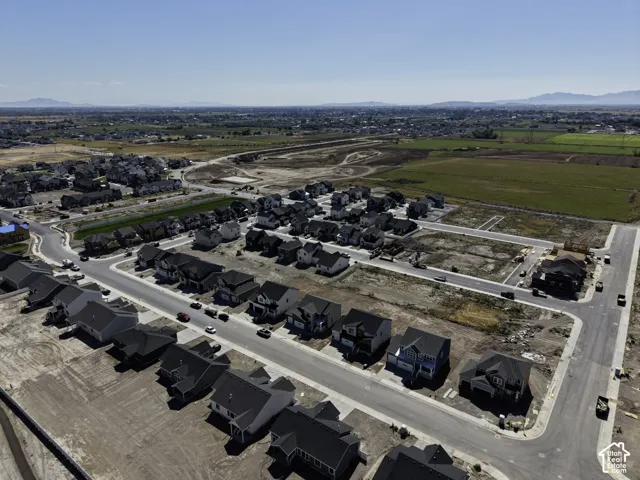 Newly developed residential community with paved streets and established homes, set against a backdrop of distant mountains and agricultural land