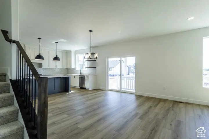 Open-concept living area featuring wood-finish flooring, a contemporary kitchen with white cabinetry and an island, a sliding glass door to the outdoors, and a modern stair railing