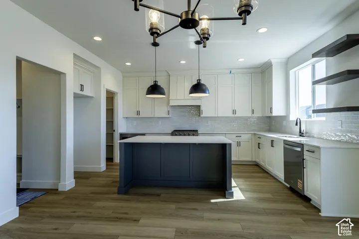 Spacious kitchen featuring an expansive center island, white cabinetry, light wood-finish flooring, a contemporary chandelier, and a subway tile backsplash