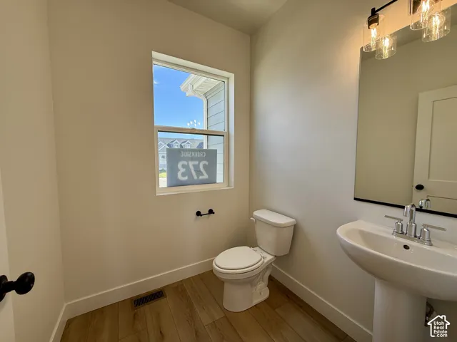 Powder room featuring wood-finish flooring, pedestal sink with chrome faucet, large rectangular mirror, and three-bulb linear vanity light