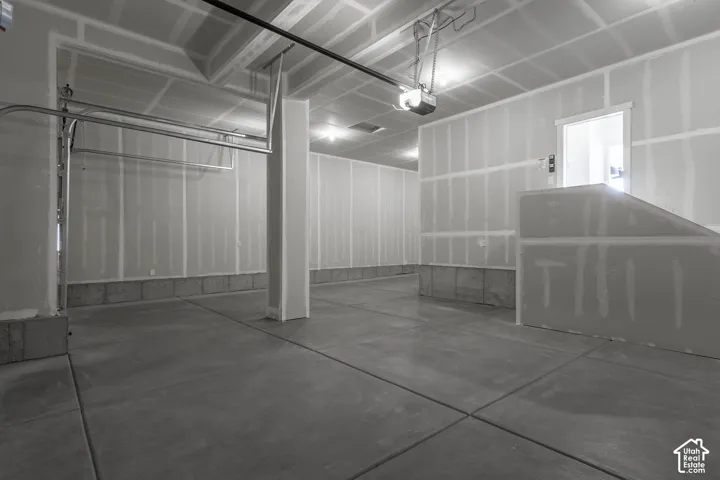 Spacious garage featuring concrete flooring, unpainted drywall, exposed ceiling joists, and an automatic garage door opener