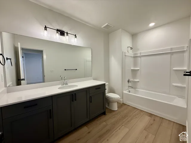Bathroom featuring a large vanity with dark cabinetry, white solid-surface countertop, full-width mirror, and wood-finish flooring