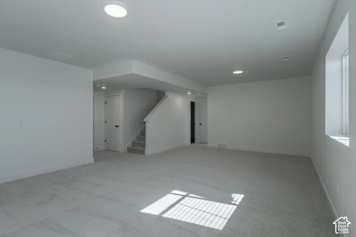 Expansive carpeted area with recessed lighting, a staircase with carpeting, and a window