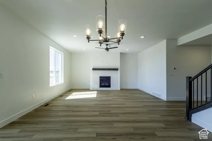 Expansive open living area featuring wood-finish flooring, a contemporary fireplace with a wood mantle, a modern chandelier, recessed lighting, and a window for natural light
