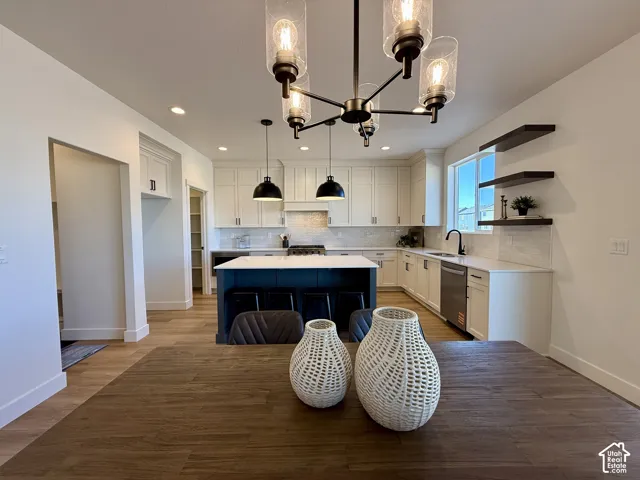 Kitchen featuring white cabinetry, center island with stone-finish countertop, wood-finish flooring, matte black pendant lighting, and floating wood shelving