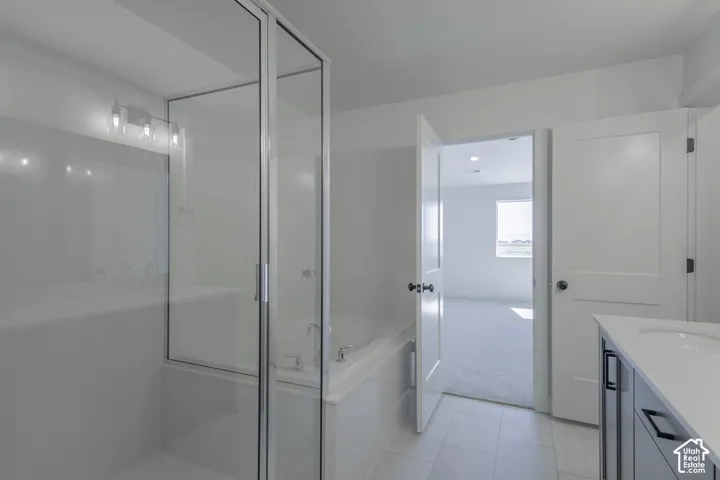 Built-in tub with glass-enclosed shower, dual-sink vanity with white countertop, and tile flooring